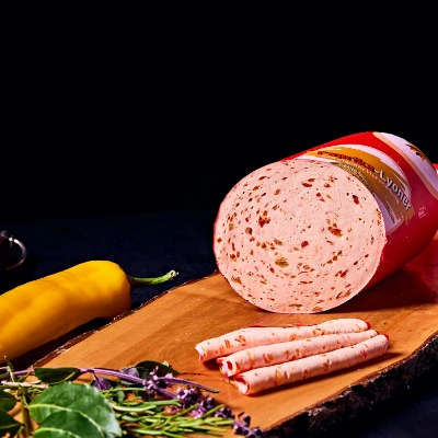Paprika-Lyoner – feinwürzige Brühwurst mit Paprikastückchen, aufgeschnitten auf Holzbrett mit gelber Paprika und Kräutern