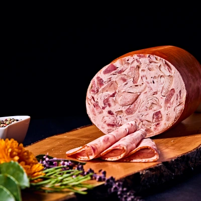 Hausgemachte Schinkenwurst – grobfleischige Wurst mit aromatischem Geschmack, aufgeschnitten auf Holzbrett mit Blütendeko