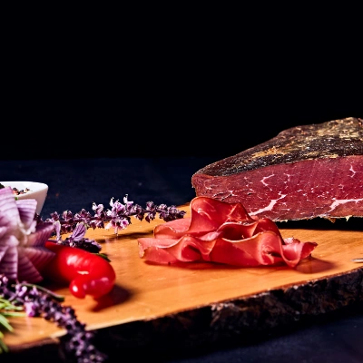 Hausgemachtes Bündnerfleisch – luftgetrocknetes Rindfleisch, hauchdünn geschnitten und angerichtet auf Holzbrett mit Tomate und Zwiebeldeko